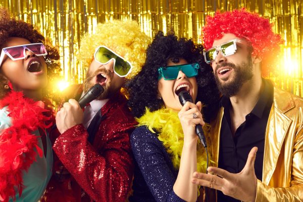 Male and female music show band with mikes performing on golden stage. Happy people dressed in funny fancy costumes having fun singing at New Year, Christmas, birthday or Halloween karaoke disco party