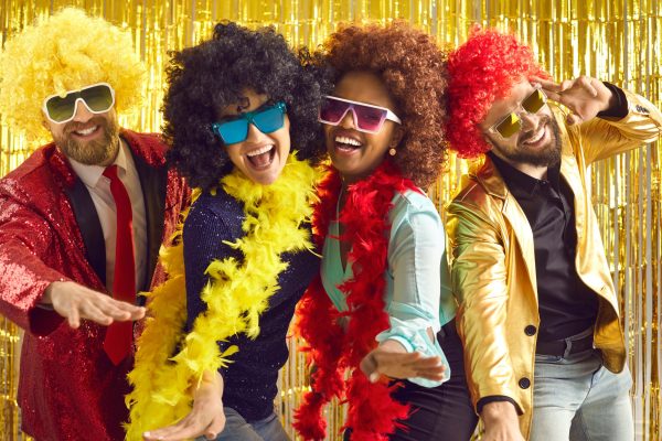 Bunch of excited young friends having fun together. Diverse group of happy people in boas, cool sunglasses and funny silly curly wigs dancing at crazy pop music nightclub disco party